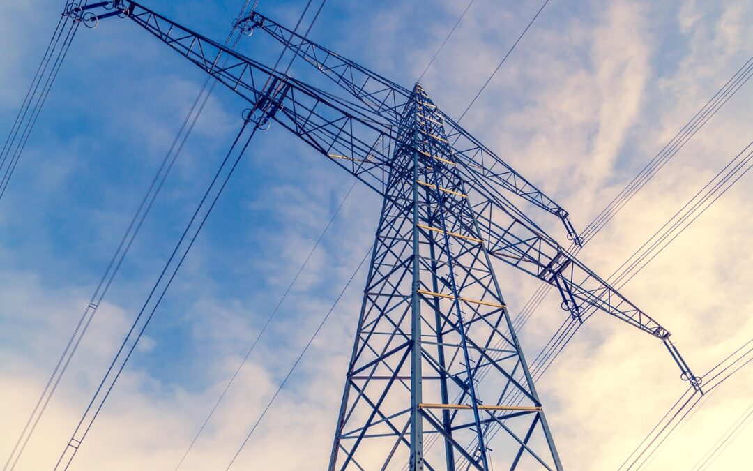 A transmission tower for power from the ground before a blue cloudy sky.