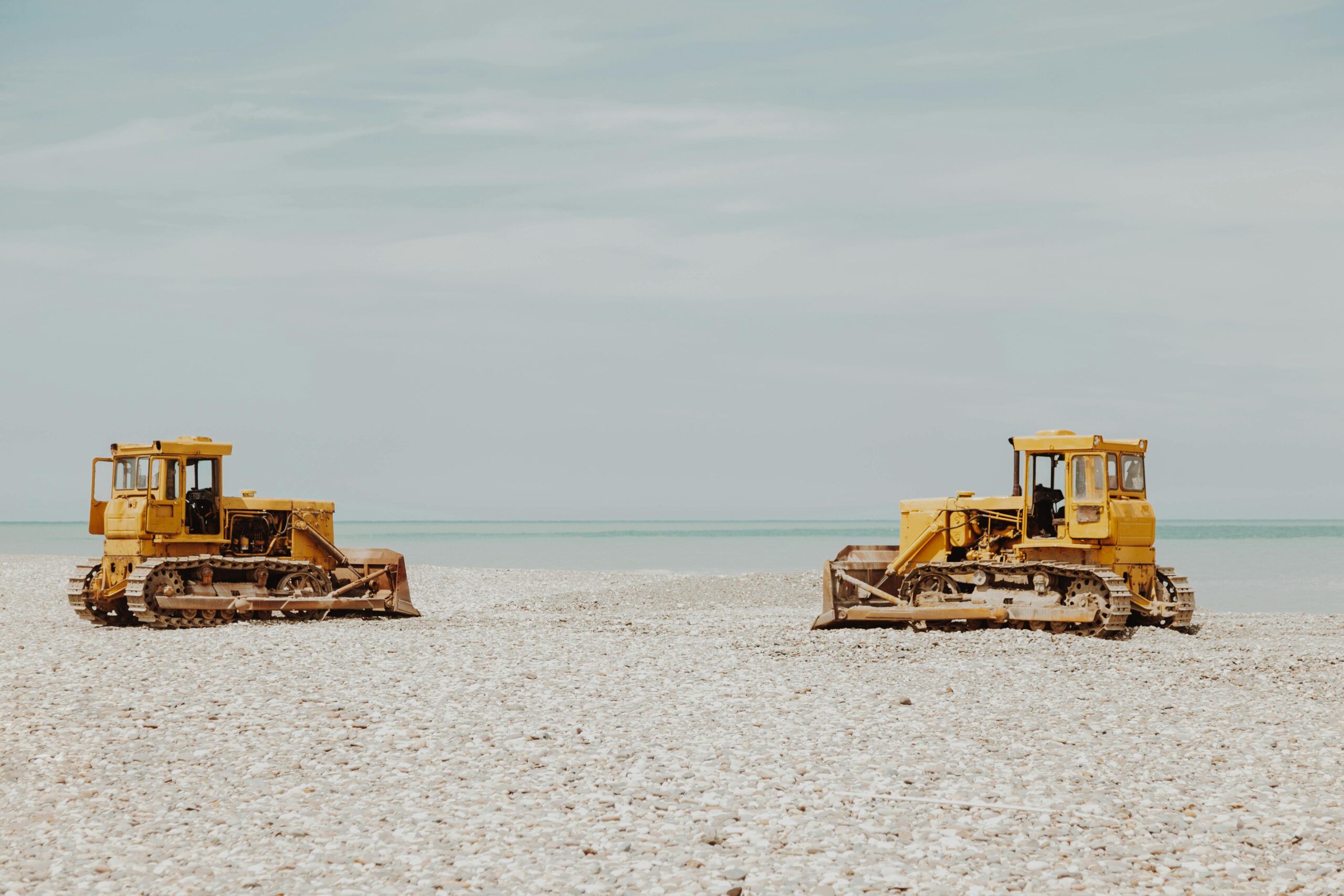 Two construction vehicles on a white-sand beach.