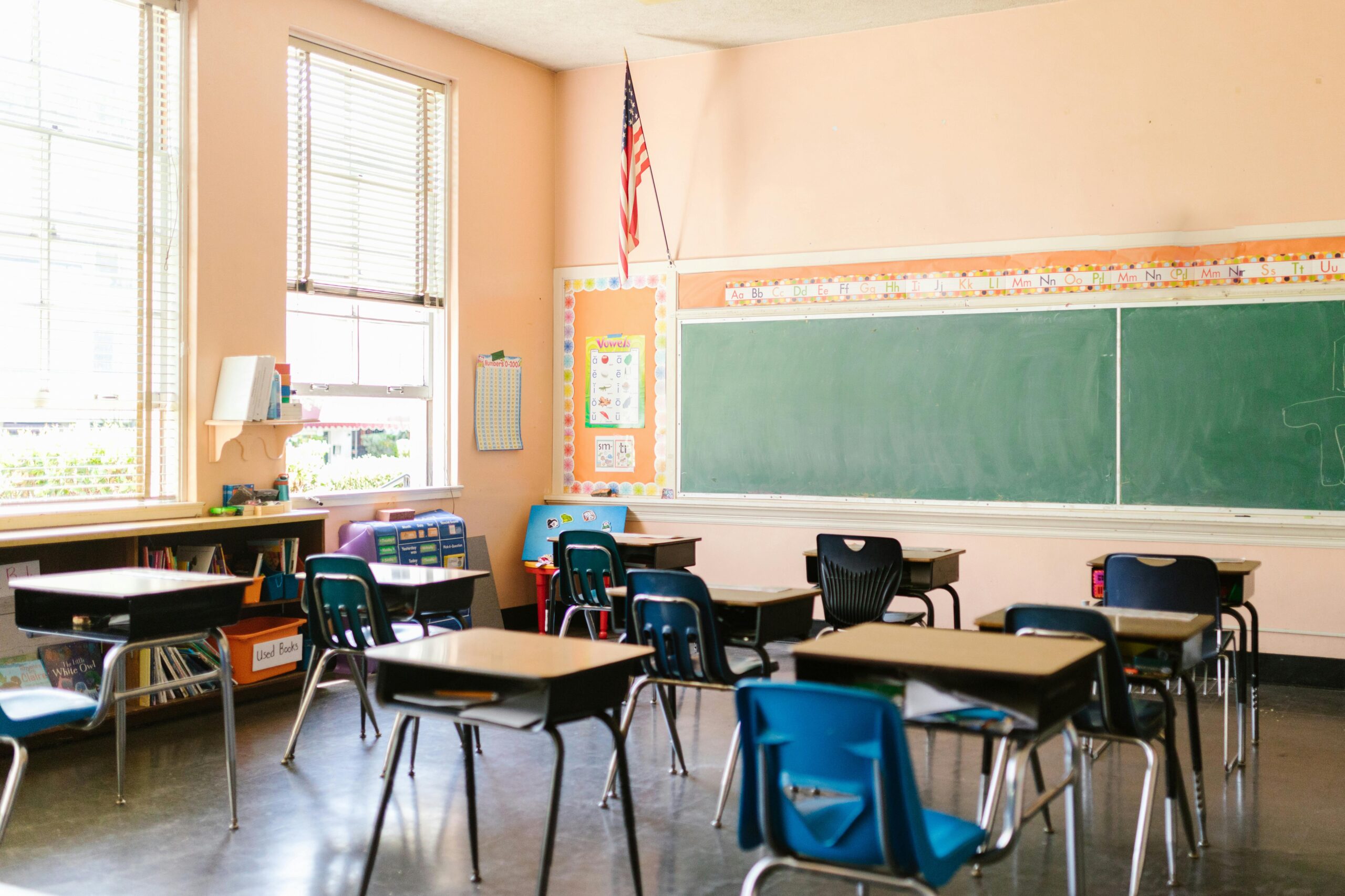 An empty classroom with a chalkboard, chairs, a desk and an American flag.