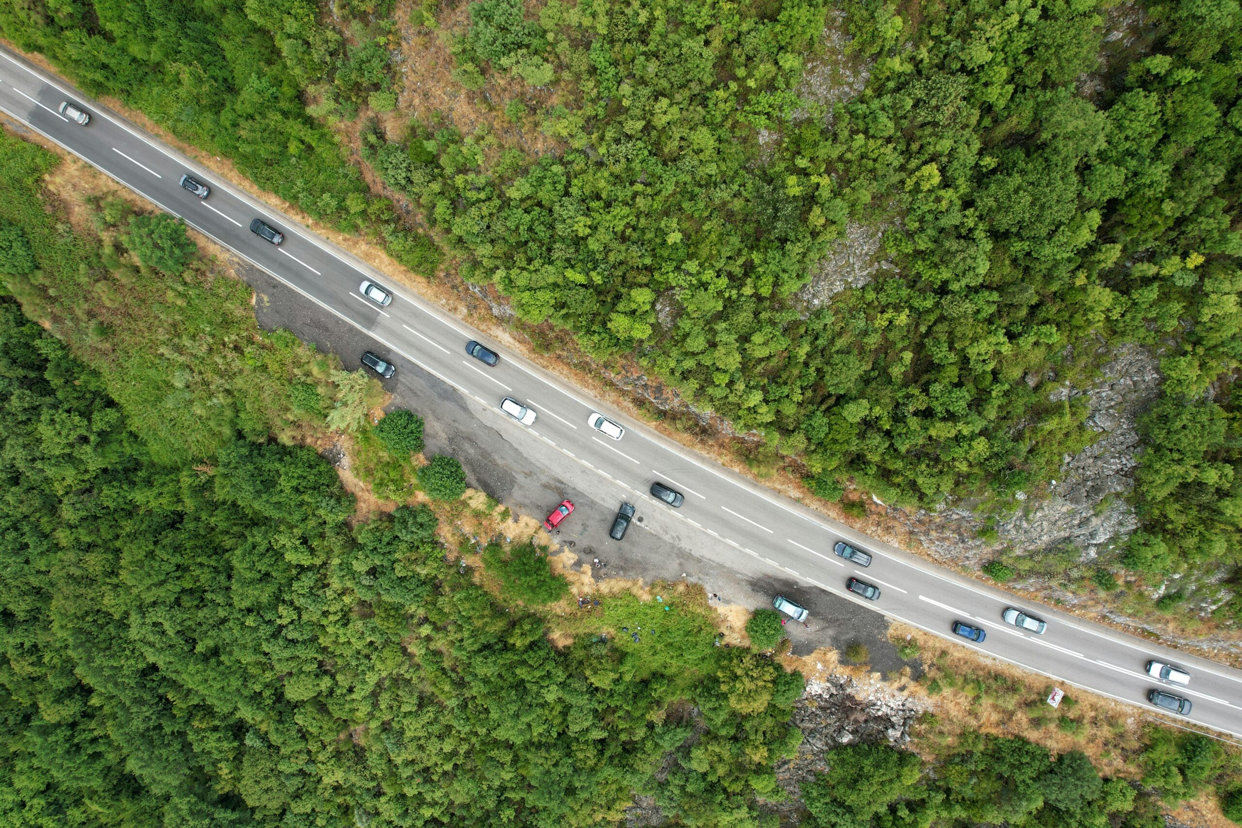 An aerial image of a highway piercing through a forest with trees lining either side of the roadway.