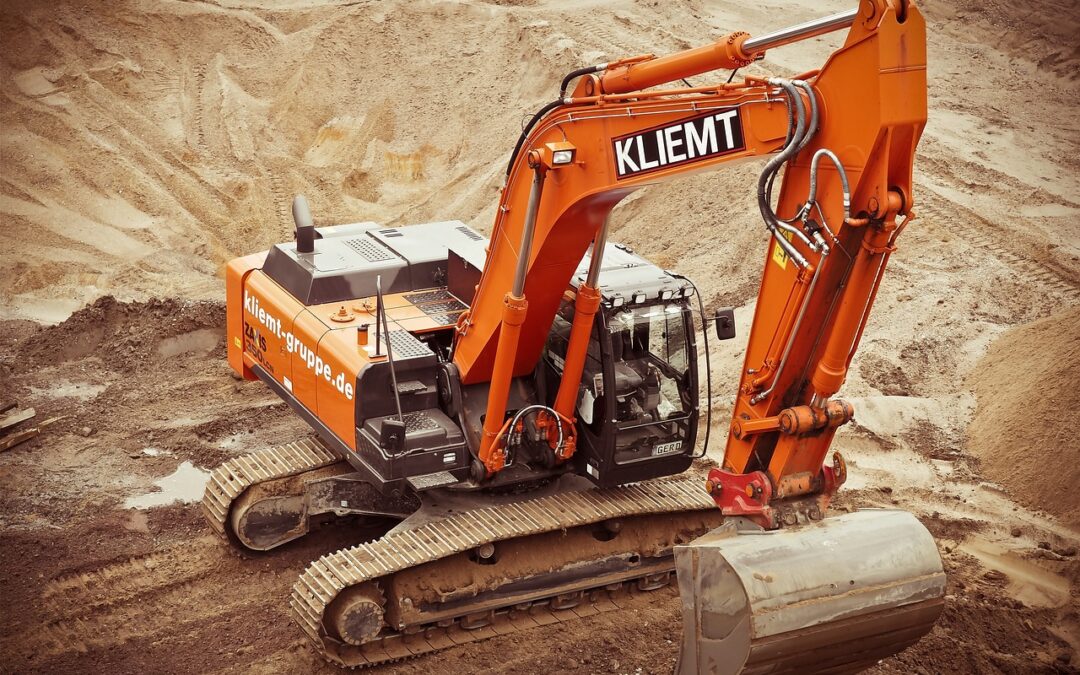 An excavator sits atop a dirt mound on a construction site.