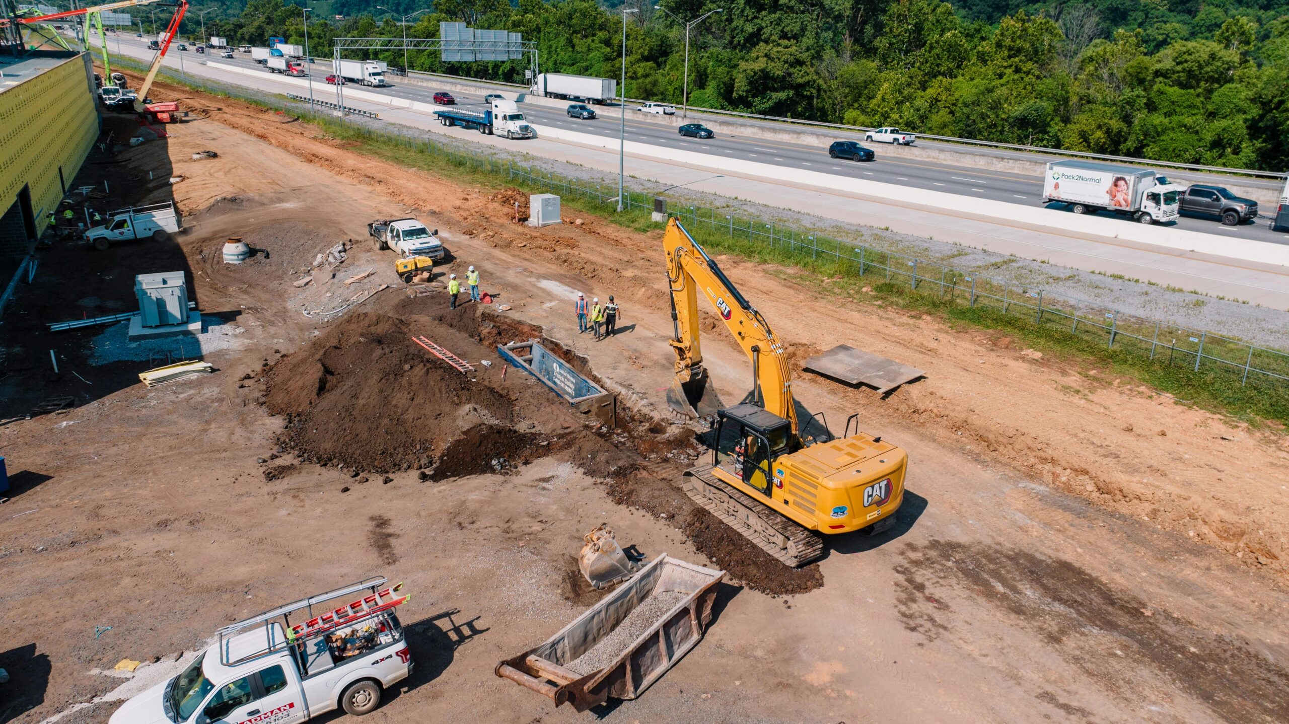 Construction vehicles on a dirt mound next to an active highway from above.