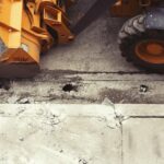 A bulldozer alongside a cracked cement curb from above.