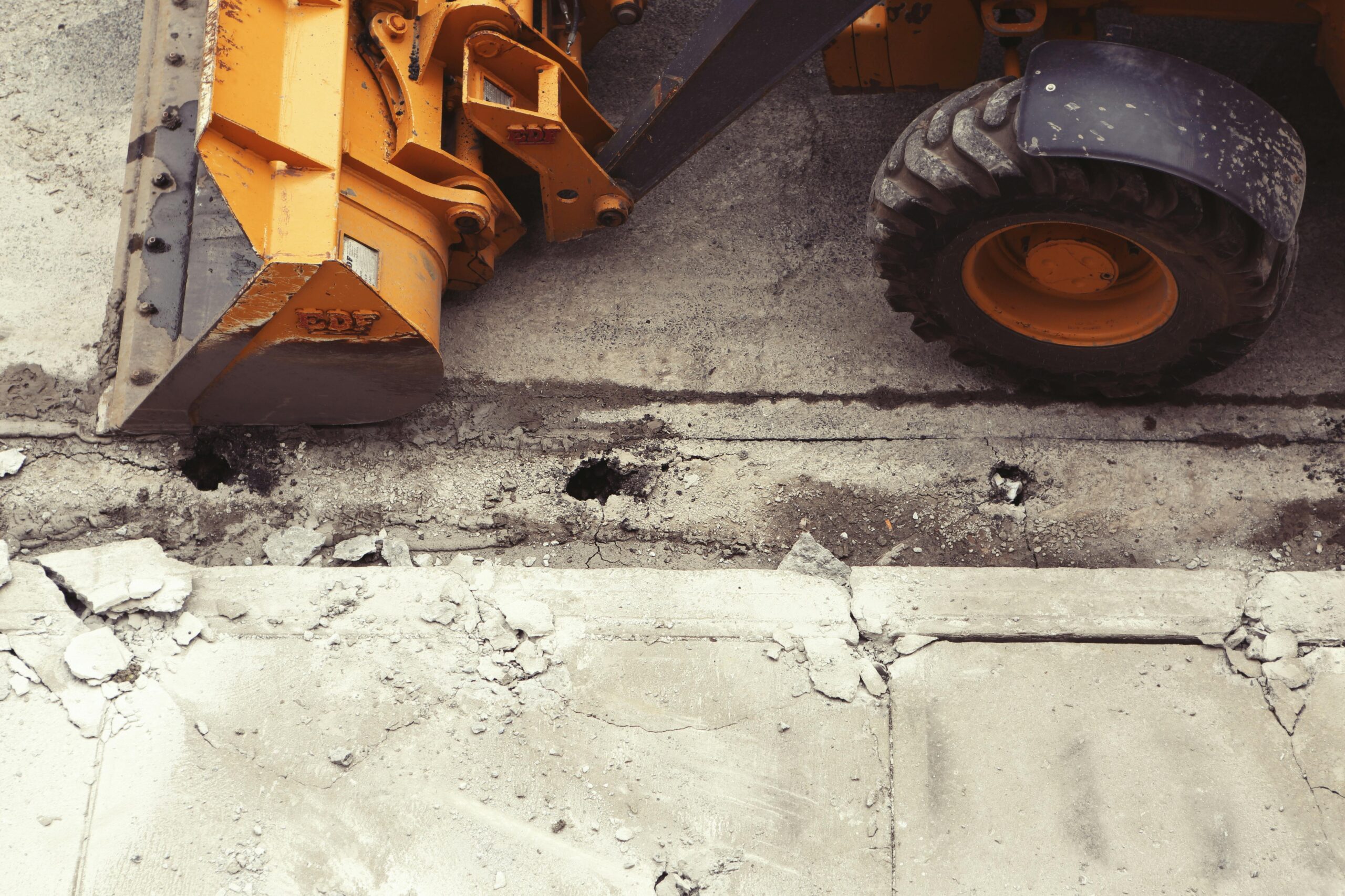 A bulldozer alongside a cracked cement curb from above.
