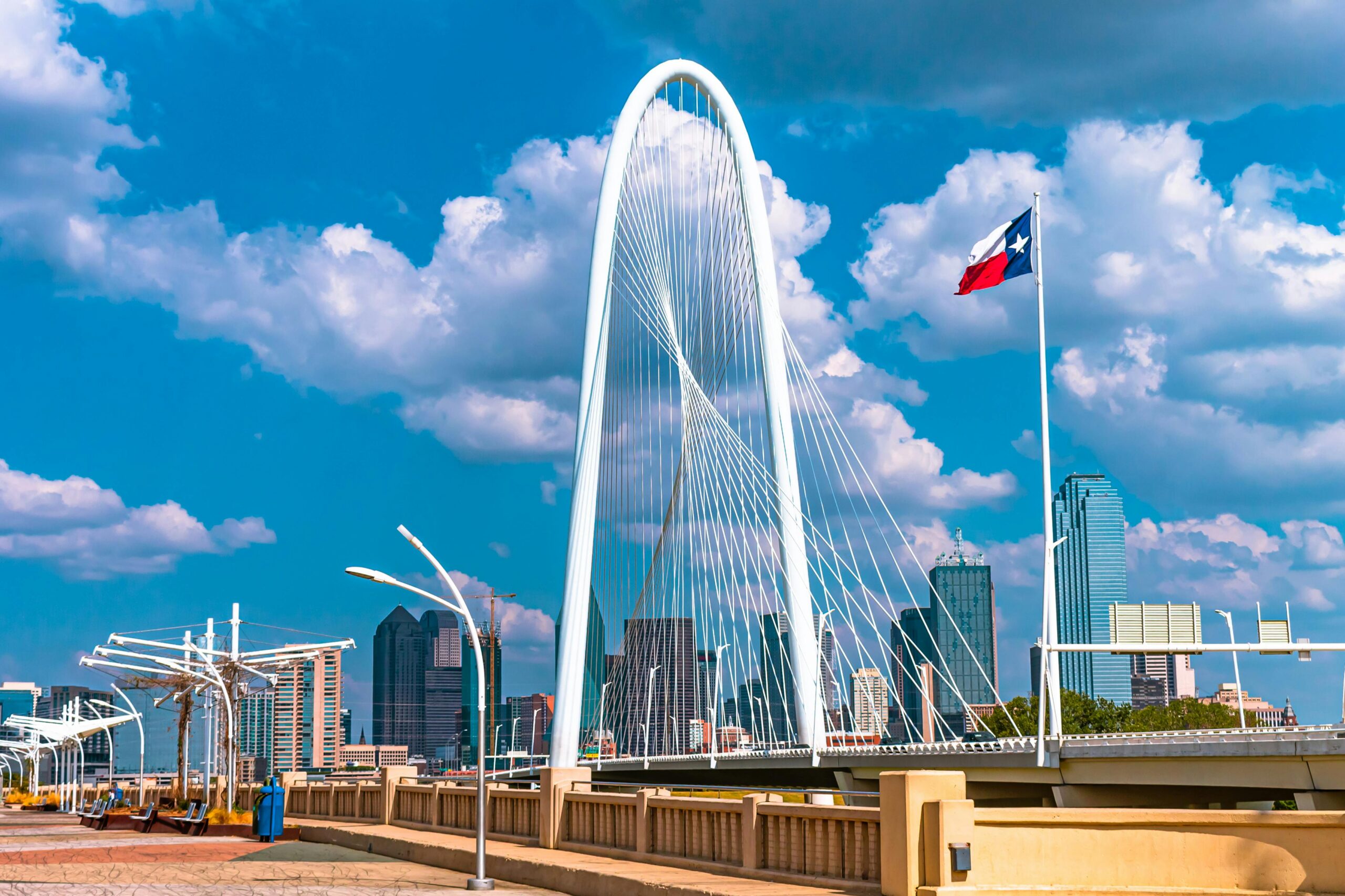 A bridge in Dallas before the Dallas skyline and a blue sky.