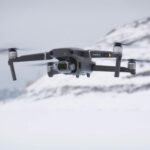 A black drone flies above a snowy background.