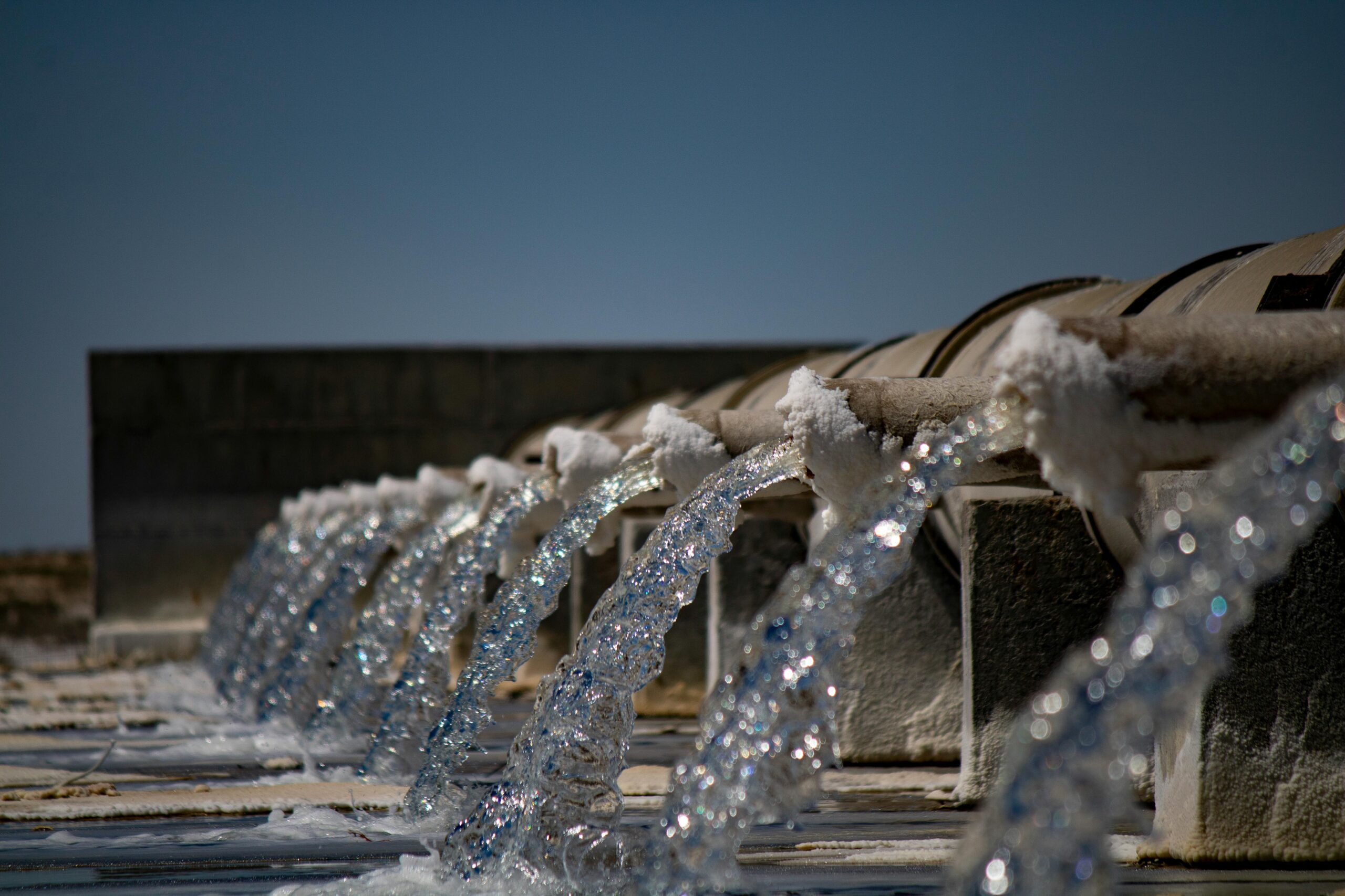 Several streams of water pour over pipes into a body of water.
