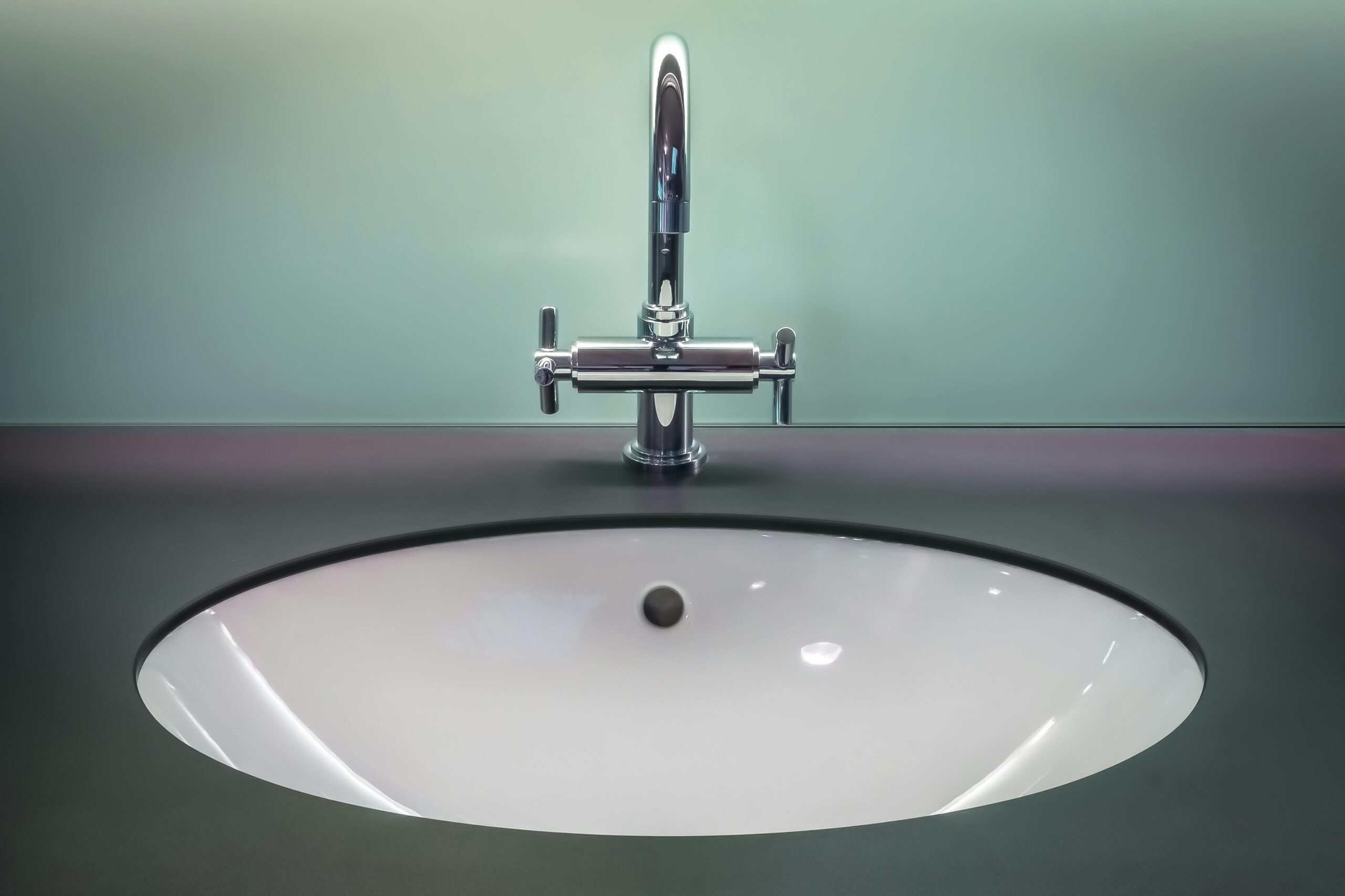 A water faucet sits untouched in a green bathroom with grey countertops.
