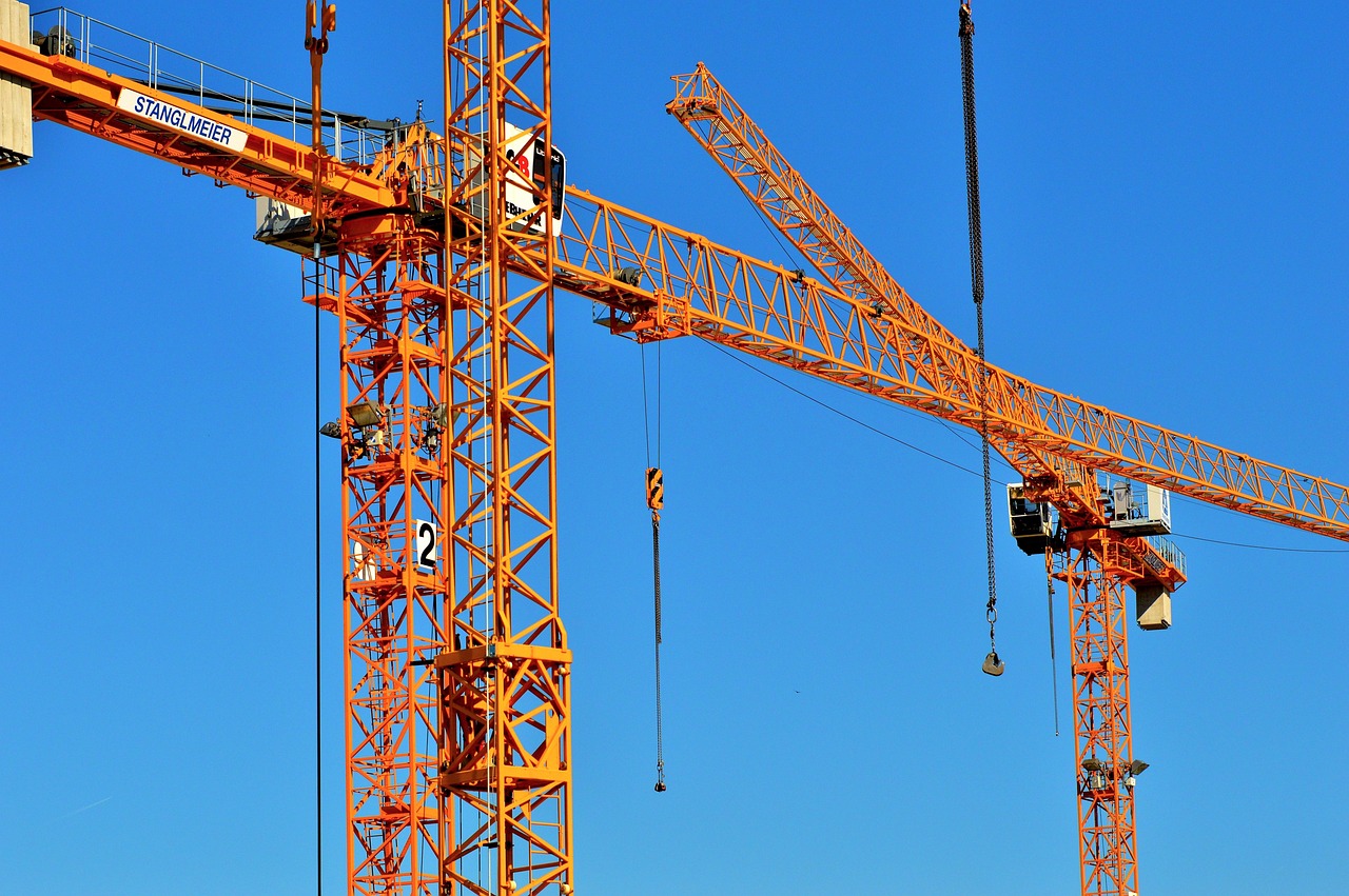 Two orange construction cranes before a blue sky.