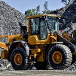 A bulldozer sits on a construction site with rocks and dirt before a blue sky.