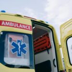 A yellow ambulance with one of the rear doors open before a cloudy sky.