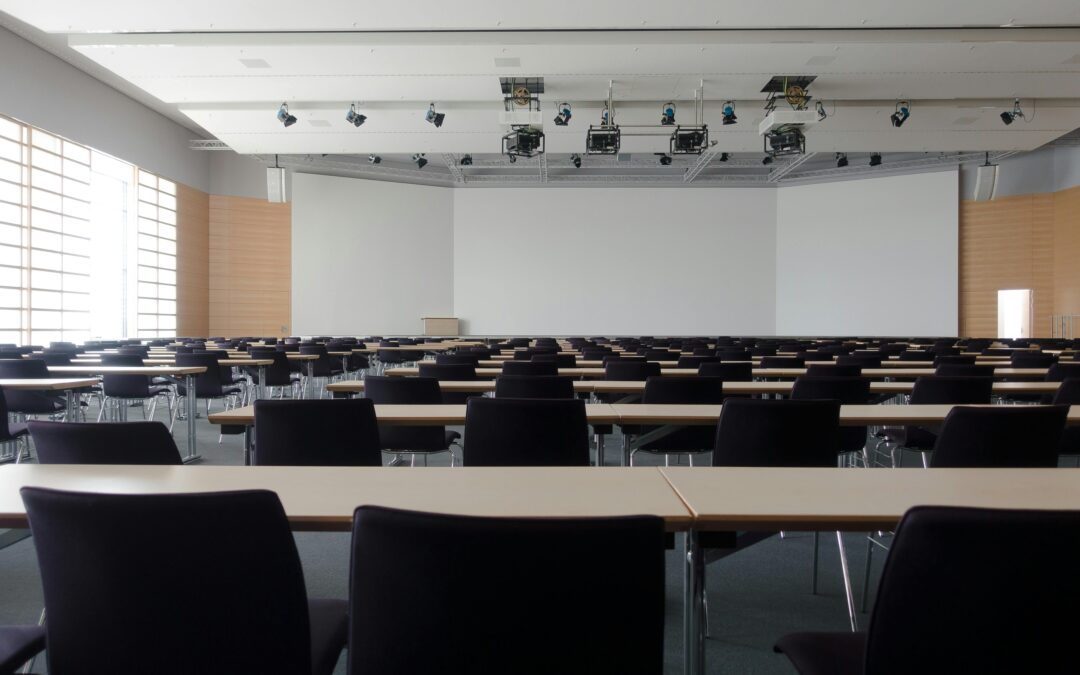 An empty classrom with chairs and desks before a large whiteboard at the front of the room.