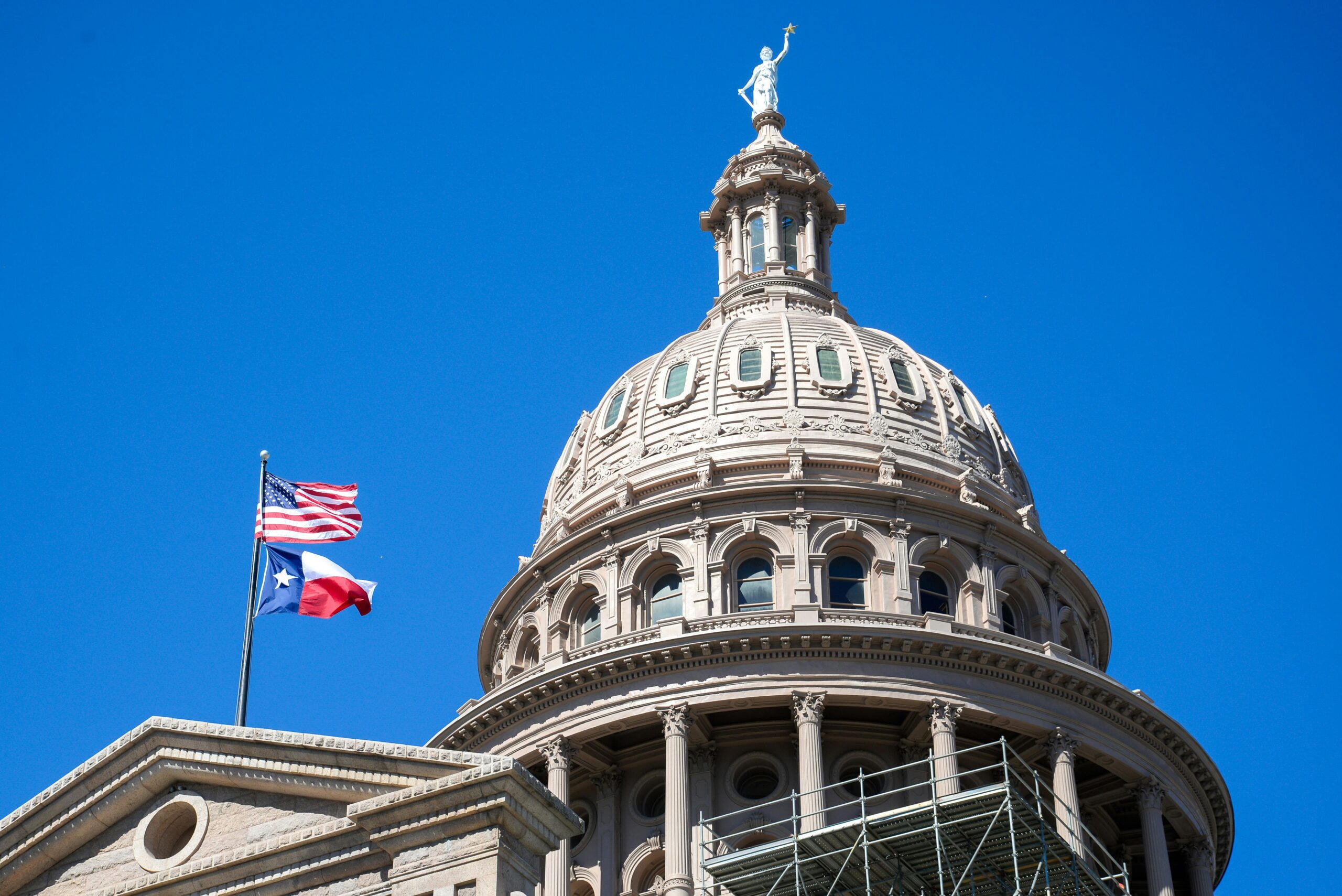 The Texas State Capitol Building with the American and Texas flags before a deep blue sky.
