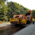 A roller machine rolls over freshly paved asphalt.