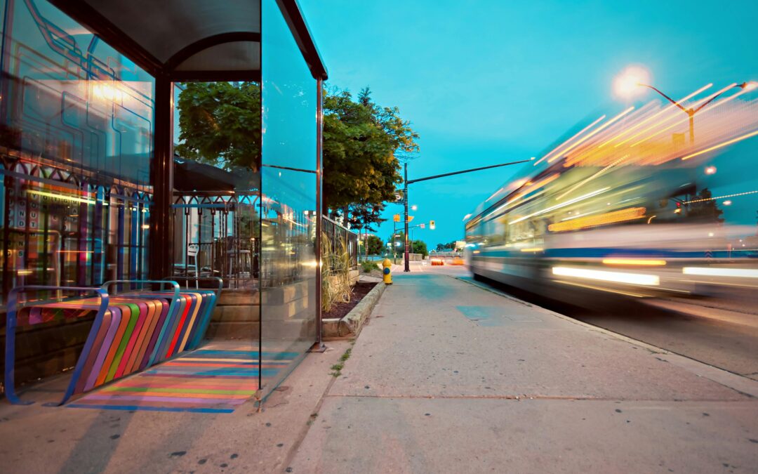 A bus zooms past a bus station with a multi-colored bench.