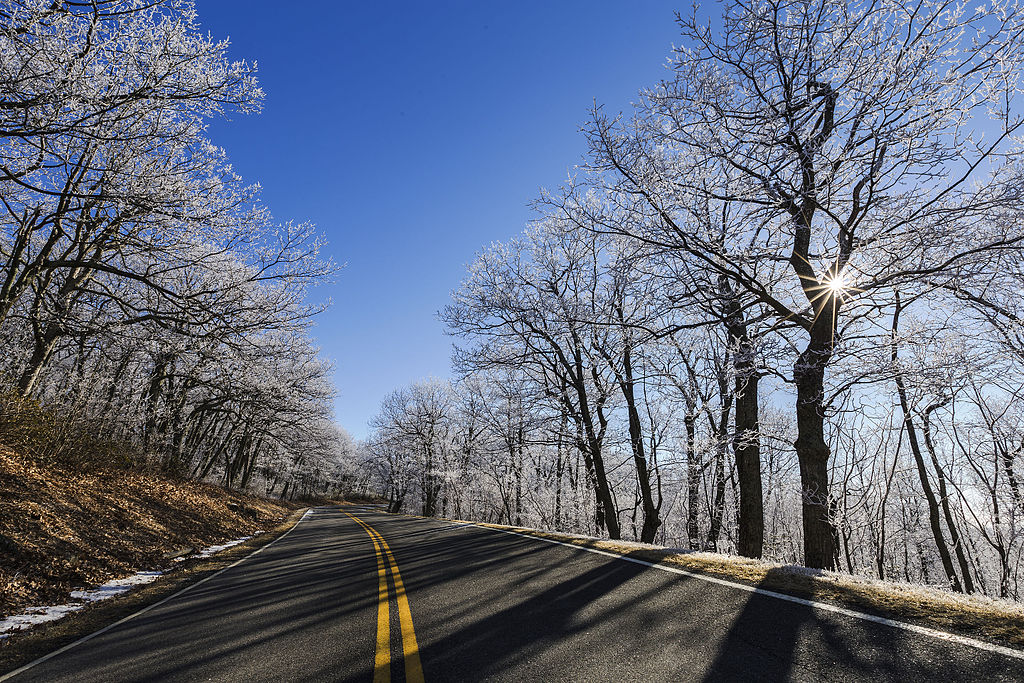 1024px-Winter_Sunburst_on_Skyline_Drive_(21852581208) A freshly paved road before nearby trees in the winter.