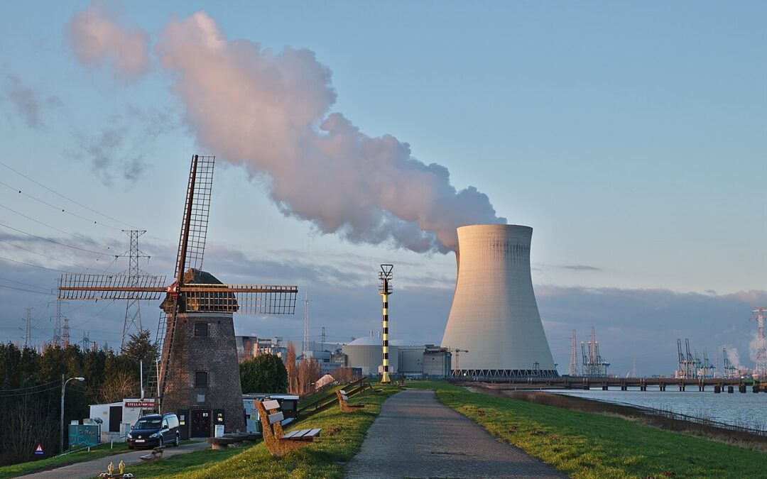 A nuclear power plant with a cooling tower in the distance after a windmill.