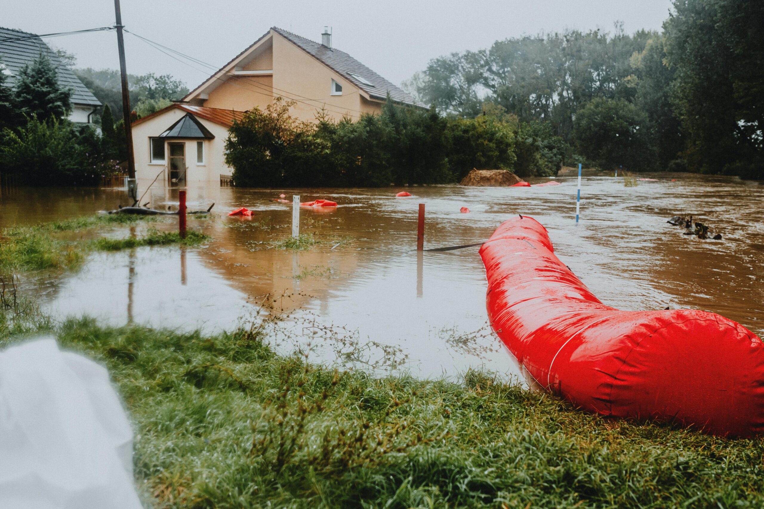Flood mitigation strategies at work in a flooded street before a house and trees.