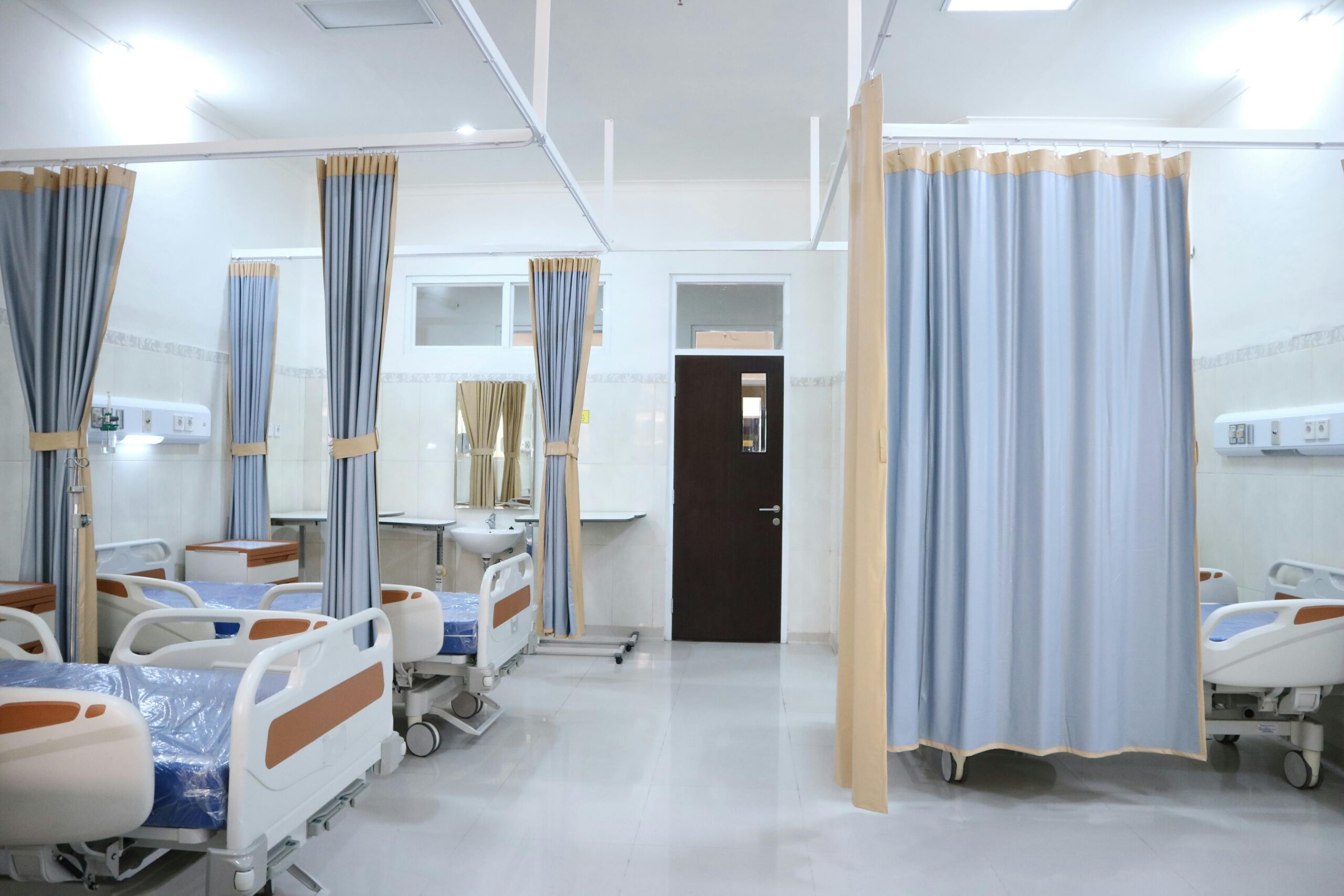 texas-rural-healthcare-investment (2) A hospital room with three beds and curtains before a closed black door.